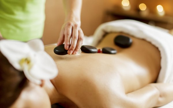 Pessoa recebendo uma massagem relaxante com pedras quentes, com pedras lisas colocadas ao longo das costas 