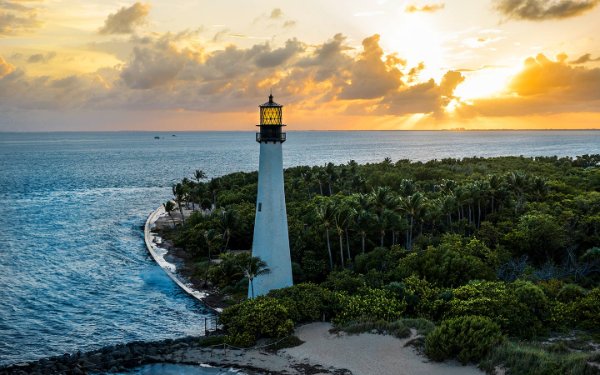 Le phare de Bill Baggs Cape Florida contre un ciel de coucher de soleil vibrant, avec des teintes d'orange se reflétant sur les eaux calmes de l'océan