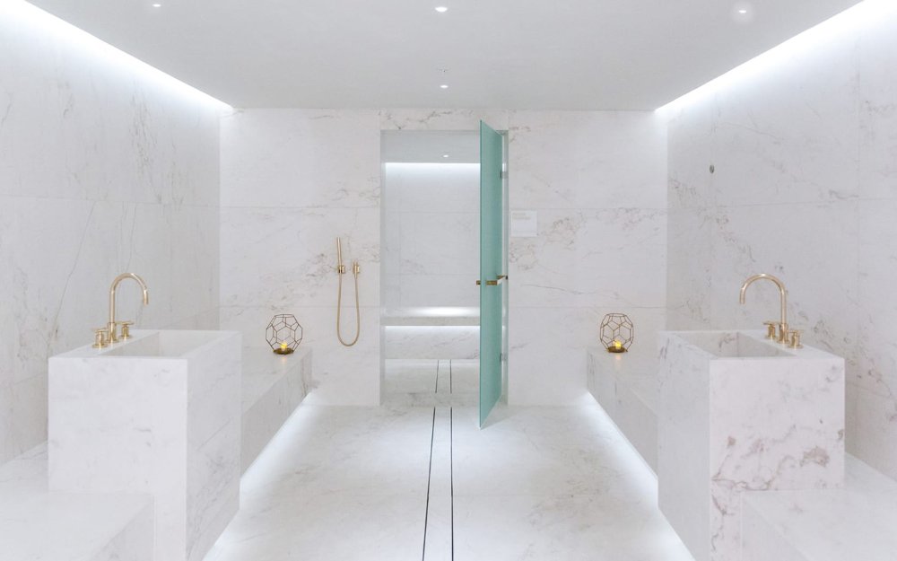 Spa à Four Seasons Hotel at The Surf Club , présentant un élégant décor en marbre avec deux lavabos, un coin salon et une douche entourée de marbre blanc.