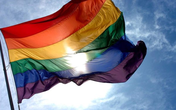 Bandeira LGBTQ tremulando no céu azul com o sol brilhando